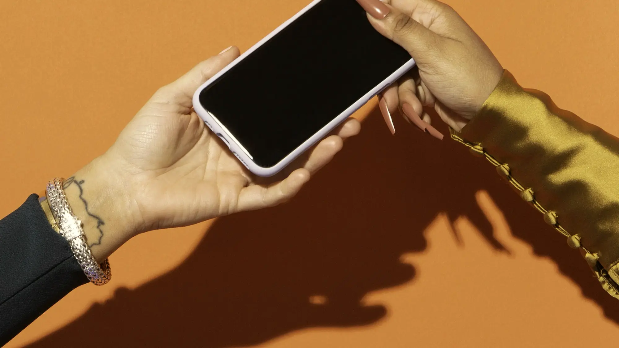 Dłoń trzymająca smartfon na ciepłym, pomarańczowym tle